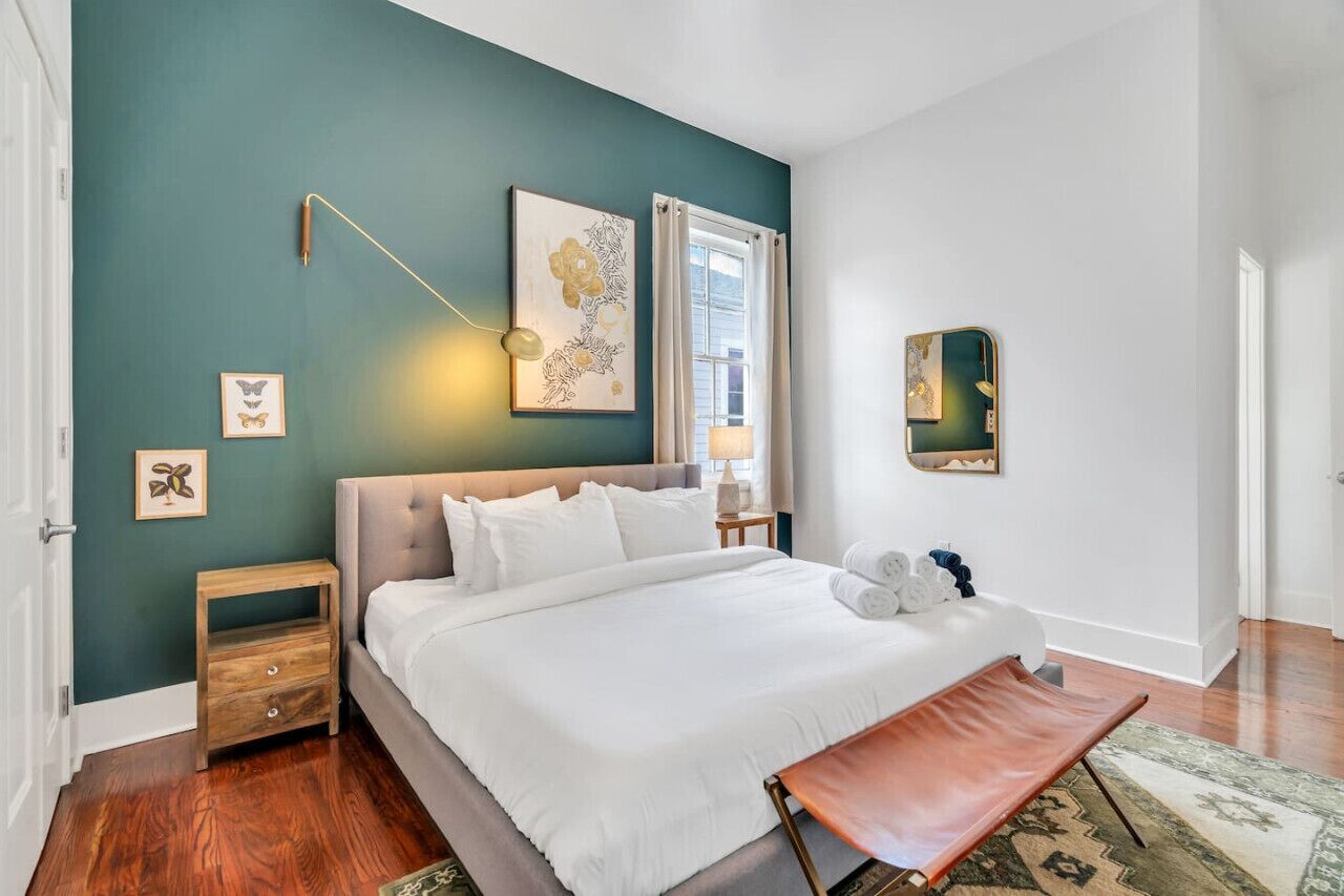 Une chambre à coucher avec un grand lit, une table de chevet, une commode, une lampe et un miroir au mur.