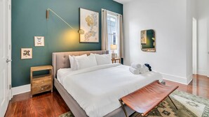 A bedroom with a large bed, a bedside table, a nightstand, a lamp, and a mirror on the wall. - Chic Magazine St. Apt | King Bed, Balcony, Parking (New Orleans)
