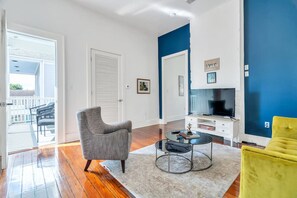 A living room with a grey armchair, a round coffee table, a yellow armchair, a television, and a white cabinet.