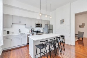 A modern kitchen with white cabinetry, stainless steel appliances, and a central island with bar stools.