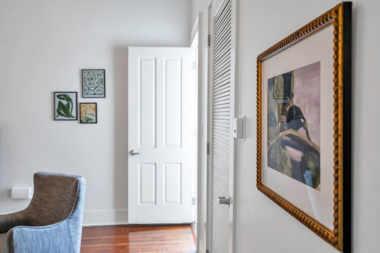 Un couloir avec une porte blanche, un tableau encadré et une chaise bleue.