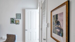 A hallway with a white door, a framed painting, and a blue chair. - Chic Magazine St. Apt | King Bed, Balcony, Parking (New Orleans)