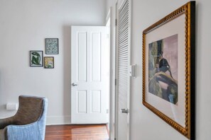 A hallway with a white door, a framed painting, and a blue chair. - Chic Magazine St. Apt | King Bed, Balcony, Parking (New Orleans)