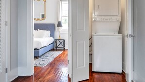 Un dormitorio con cama, espejo, lámpara y lavadora.