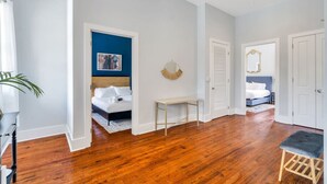 Un dormitorio moderno con suelo de madera, una cama con ropa blanca, una mesita de noche y un espejo en la pared.