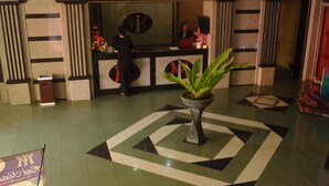 Vestíbulo con mostrador de recepción, una planta en maceta y un diseño geométrico en el suelo.