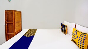 Una habitación con un armario de madera, una cama con ropa de cama blanca y almohadones con diseños geométricos.