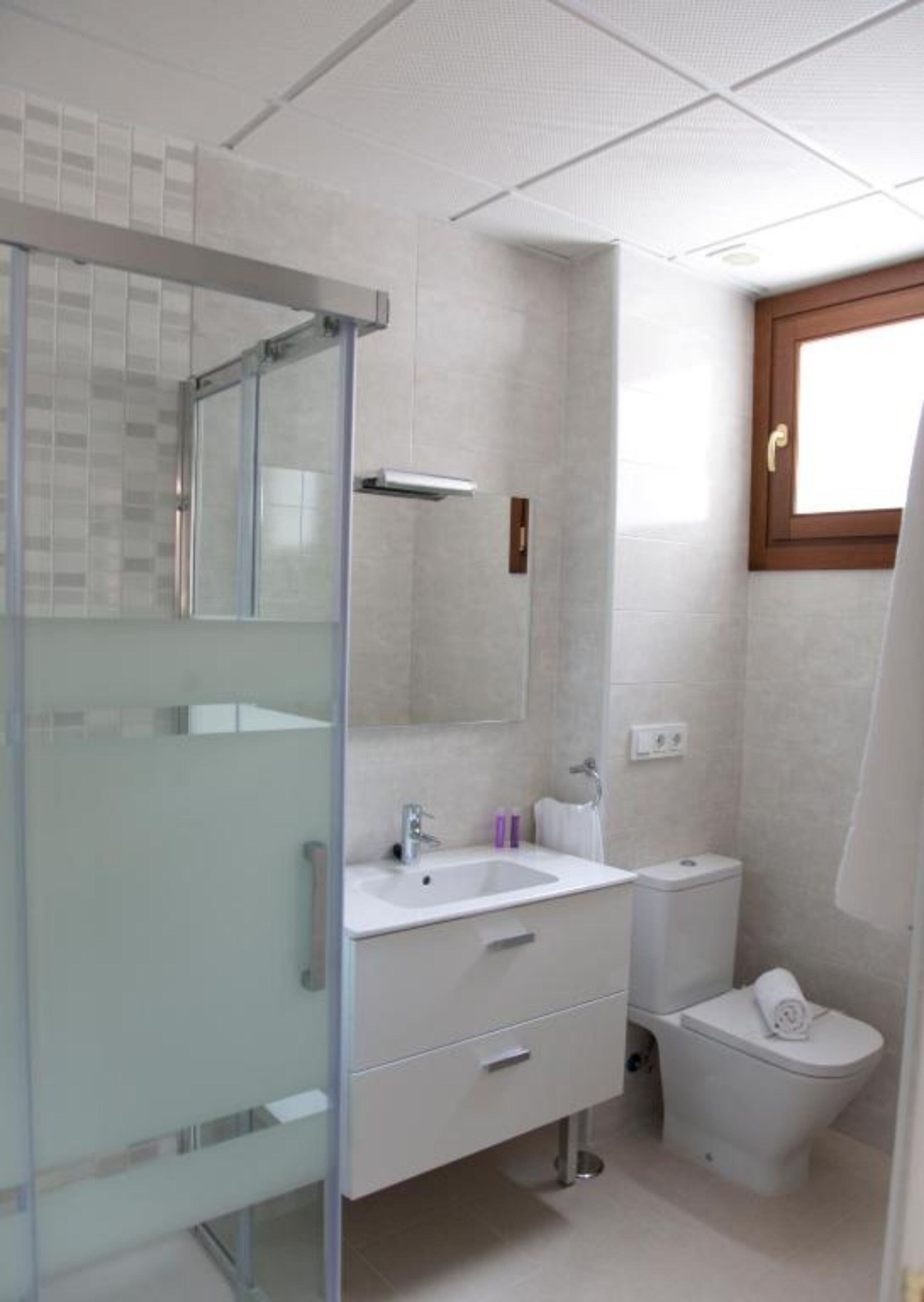 Une salle de bain moderne avec une douche à parois de verre, un lavabo blanc, des toilettes et une fenêtre avec un cadre en bois.