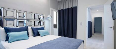 A modern bedroom with a large bed, a mirror with geometric frames, and a view of a hallway.
