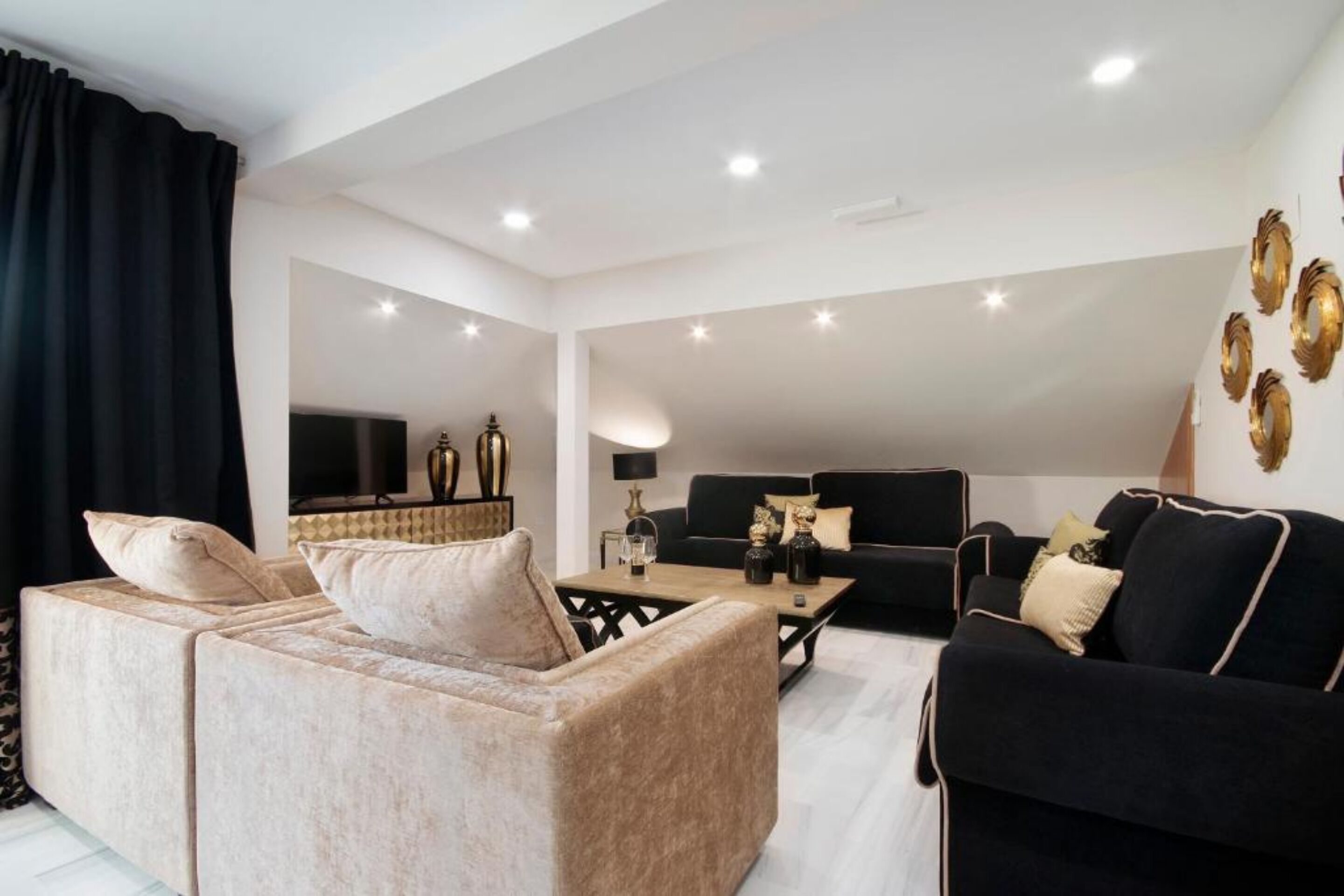 En moderne stue med en beige sofa, en sort sofa og et sofabord. Der er pyntegjenstande på sofabordet og en sort lampe ved siden af.