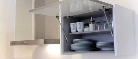 A kitchen with a built-in cabinet containing white cups, plates, and a coffee maker.