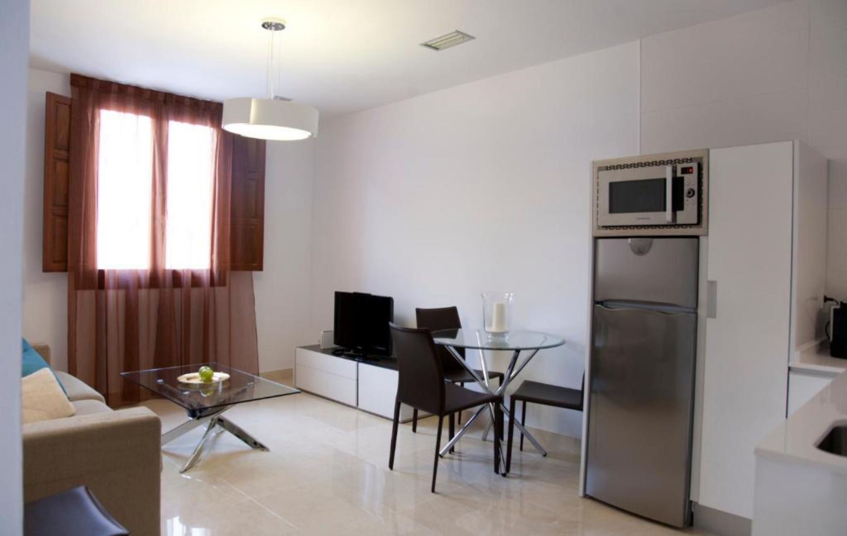 A modern kitchen with a microwave, refrigerator, and dining area with a glass table and chairs.