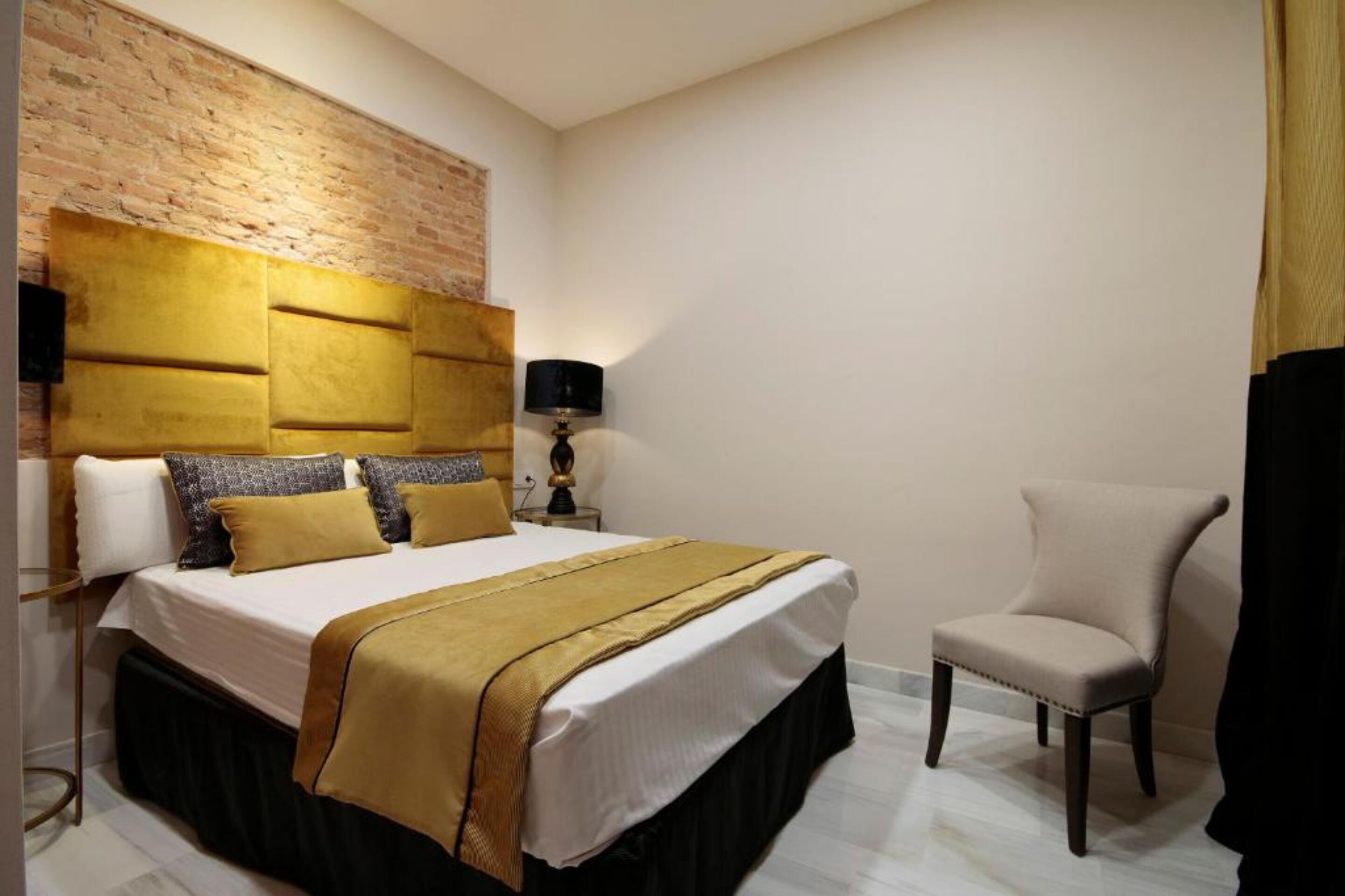 Una camera d'albergo con un letto grande, una parete decorata in mattoni, una lampada e una poltrona.