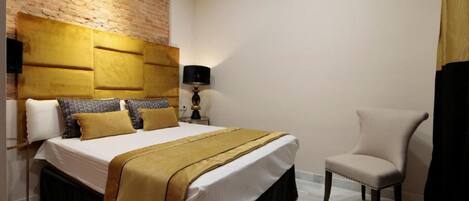 Una camera d'albergo con un letto grande, una parete decorata in mattoni, una lampada e una poltrona.
