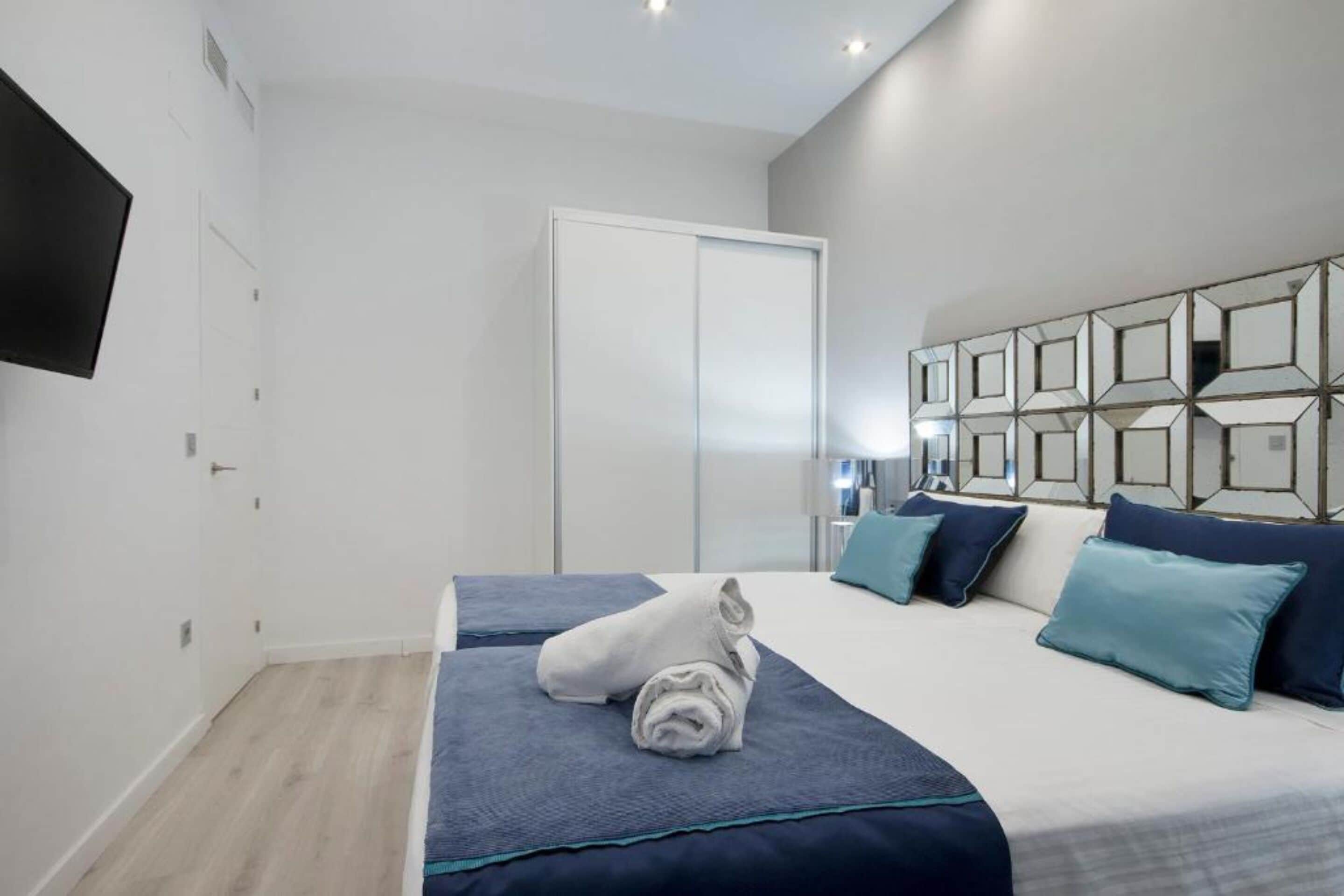 A modern hotel room with a large bed, a wardrobe, and a TV mounted on the wall.