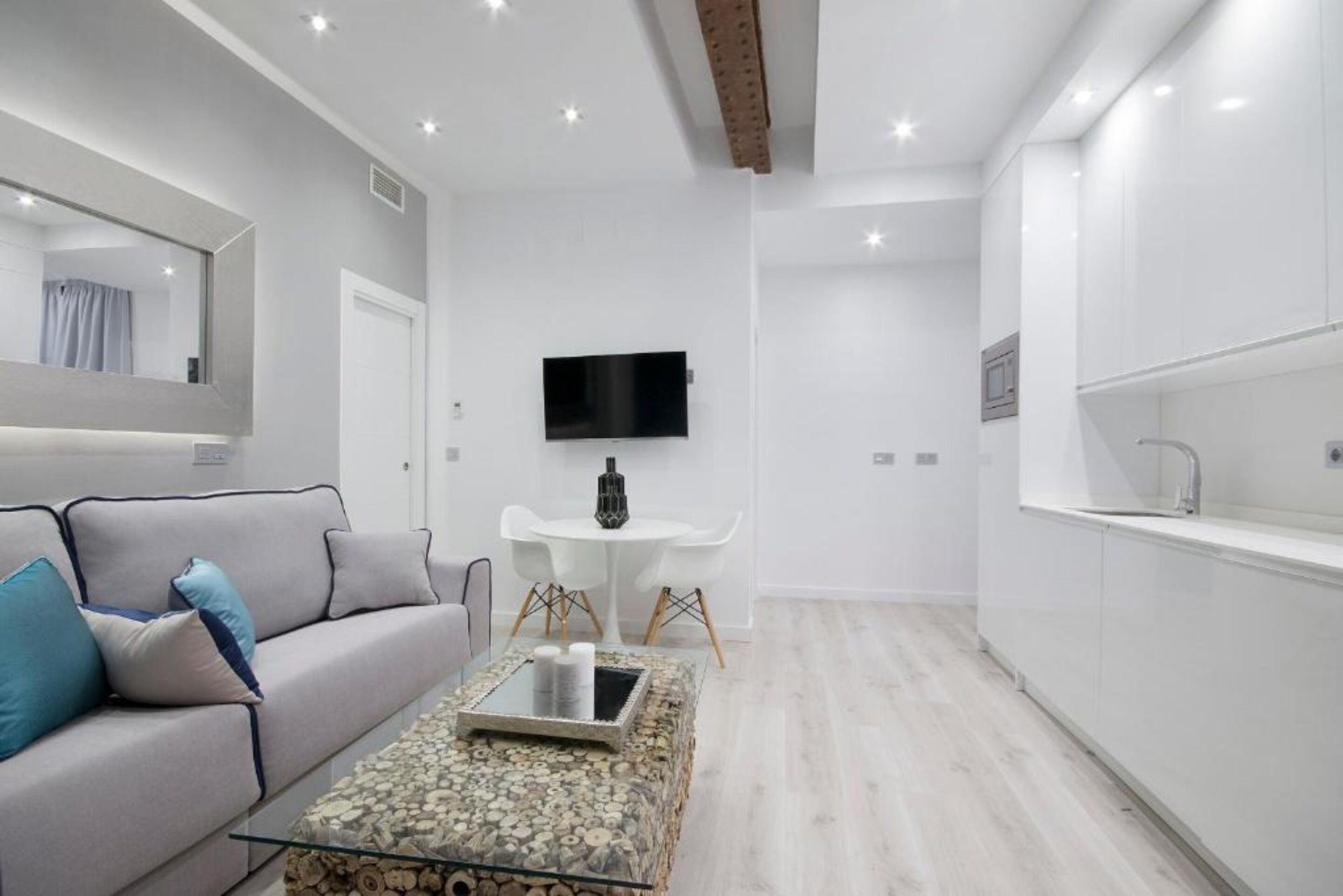A modern living room with a sofa, a coffee table, a TV, and a small dining table.