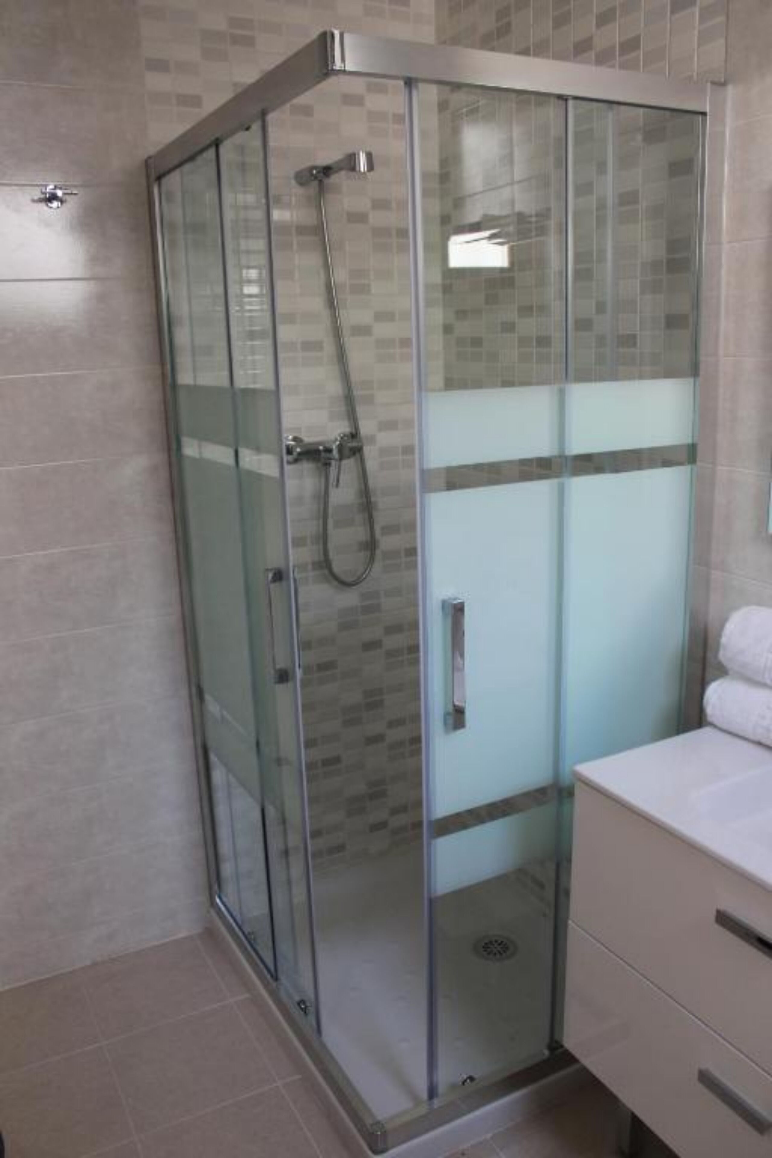 A modern bathroom with a glass-enclosed shower, a white sink, and a tiled floor.