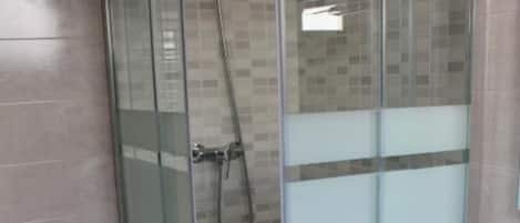 A modern bathroom with a glass-enclosed shower, a white sink, and a tiled floor.
