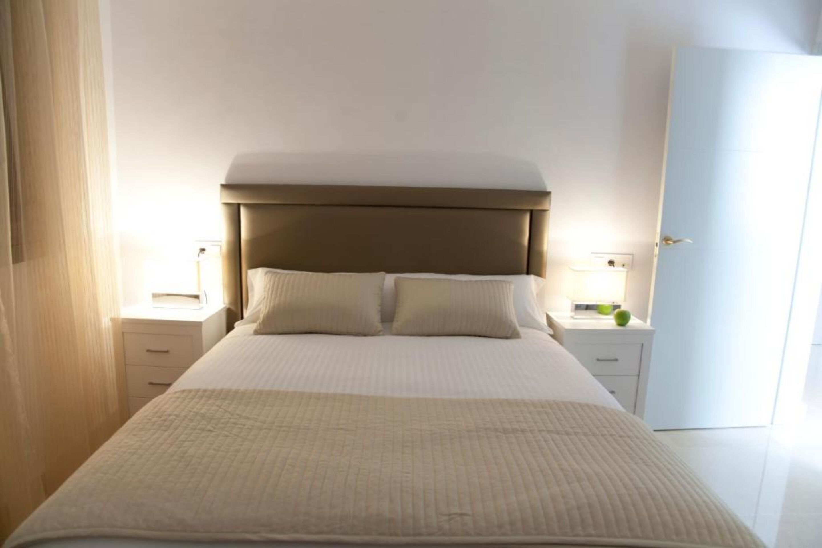 A neatly made bed with a headboard, two bedside tables with lamps, and a door to the right.