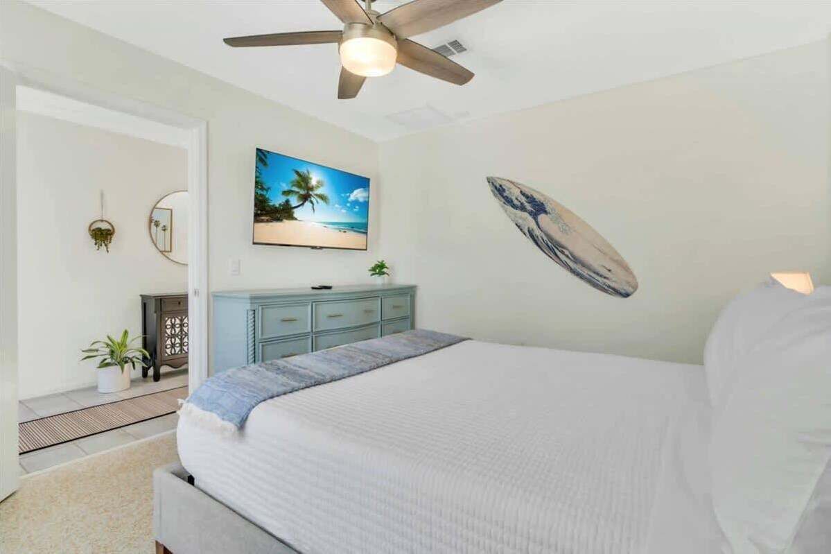 A bedroom with a bed, a ceiling fan, a TV, a surfboard decoration, and a dresser.