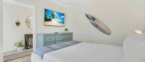 A bedroom with a bed, a ceiling fan, a TV, a surfboard decoration, and a dresser.