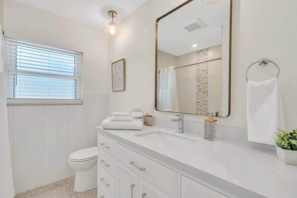A modern bathroom with a white vanity, a large mirror, a towel rack, and a potted plant. - Coastal Studio Getaway|5 Min to Beach|Pool (Nokomis)