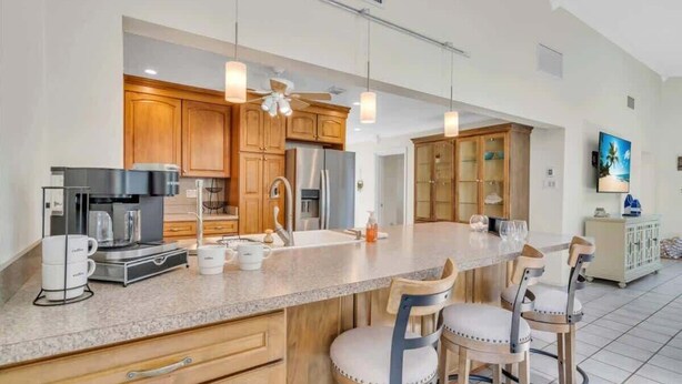 Une cuisine moderne avec des meubles en bois, un grand îlot central doté de tabourets, une machine à café et un réfrigérateur.