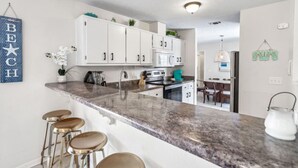 Une cuisine moderne avec des meubles blancs, un plan de travail en granit et un coin bar équipé de tabourets.