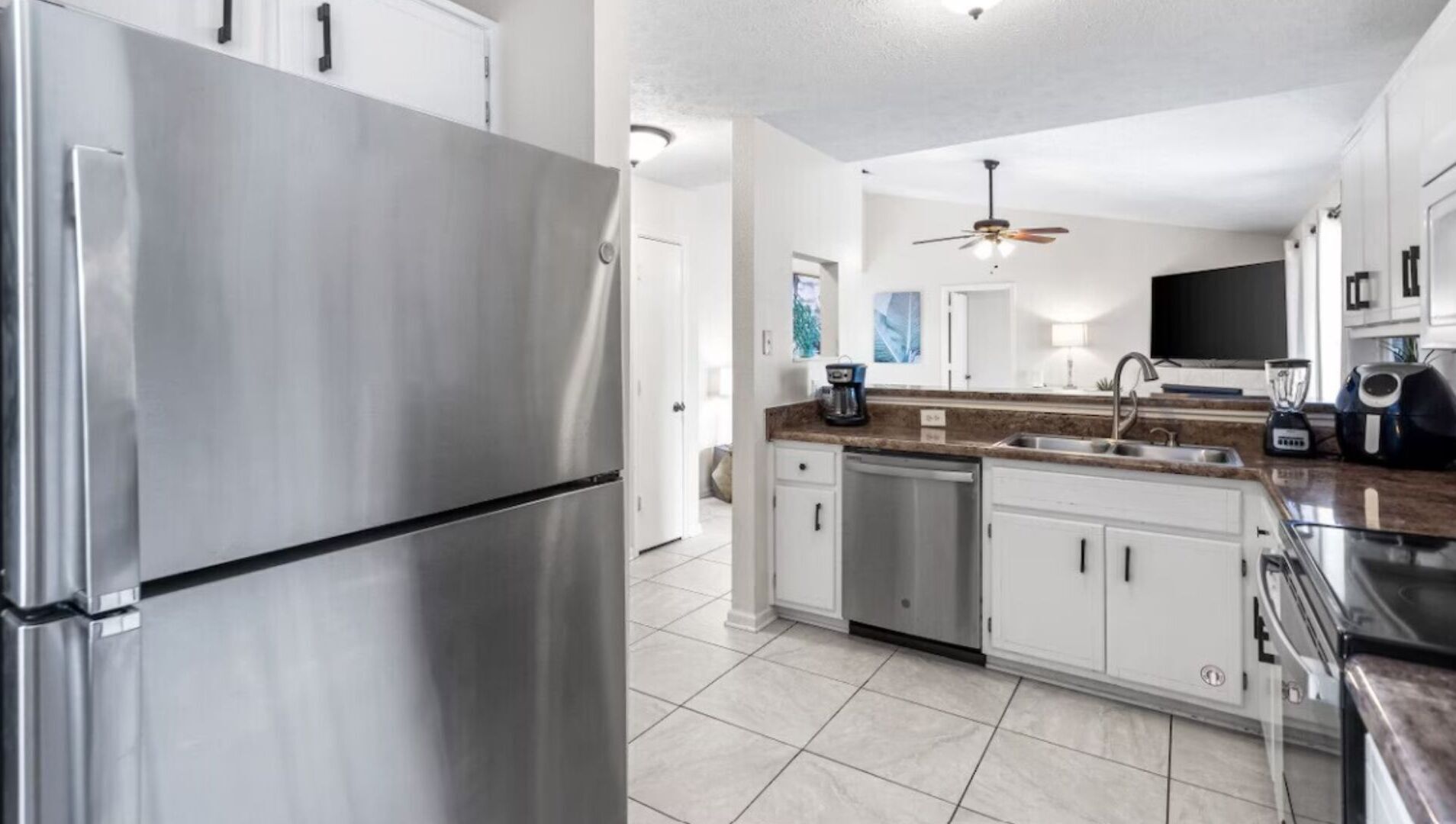 A modern kitchen with stainless steel appliances, white cabinetry, and a tiled floor.