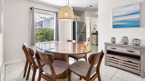 Un espace repas moderne avec une table ronde en verre, des chaises en bois et un luminaire suspendu.