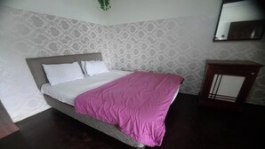 Una cama bien hecha con una colcha blanca y rosa en una habitación con papel tapiz estampado y suelo de madera oscura.