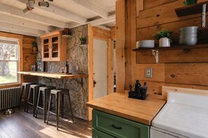 Una cocina rústica con paredes de madera, una pared de acento de piedra, taburetes de bar, una encimera y un refrigerador blanco.