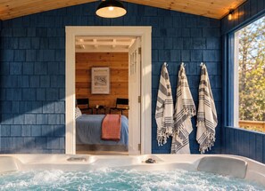 Una habitación con techo de madera, pared azul, cama con colcha azul, puerta blanca y bañera de hidromasaje con agua.