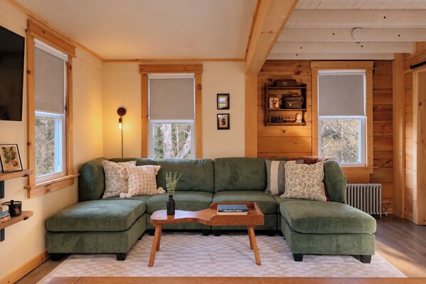 A cozy living room with a green sectional sofa, a wooden coffee table, and a bookshelf against the wall.