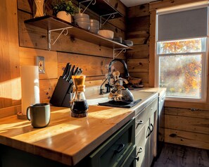 Una cocina con armarios de madera, un lavamanos y un ventanal con vistas a árboles otoñales.