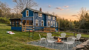 Ein blaues Haus mit Terrasse, Sitzgelegenheiten im Freien und einem Feuerkorb.