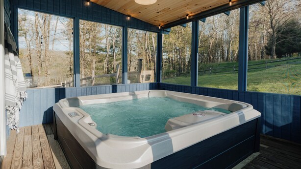 A hot tub in a wooden deck with large windows overlooking a grassy area.