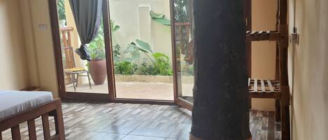 A room with a wooden bench, a pillar with a rope, and a view through a glass door to an outdoor area with plants.