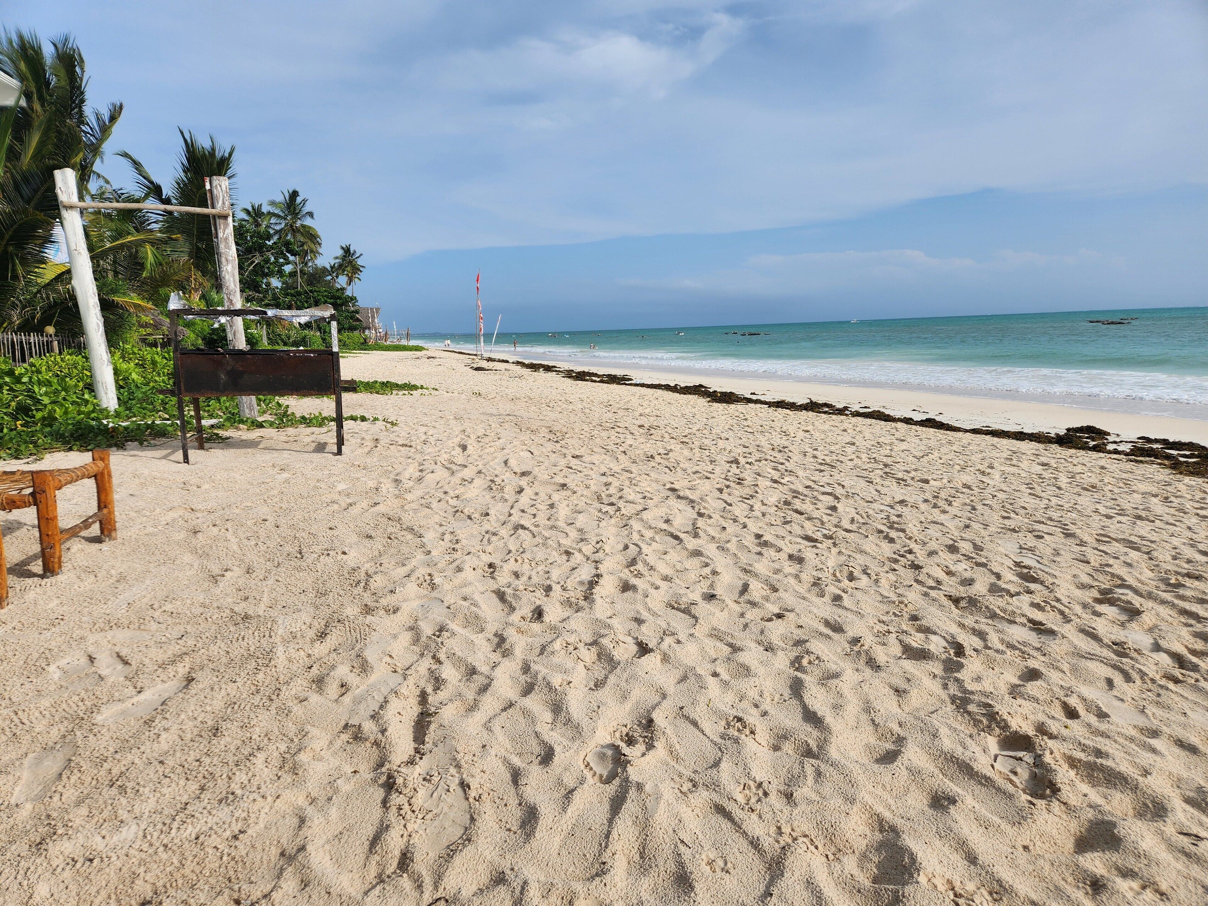 A sandy beach with footprints, a wooden bench, and a metal bench.