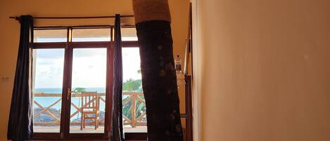 A room with a large wooden door leading to a balcony with a view of the sea.
