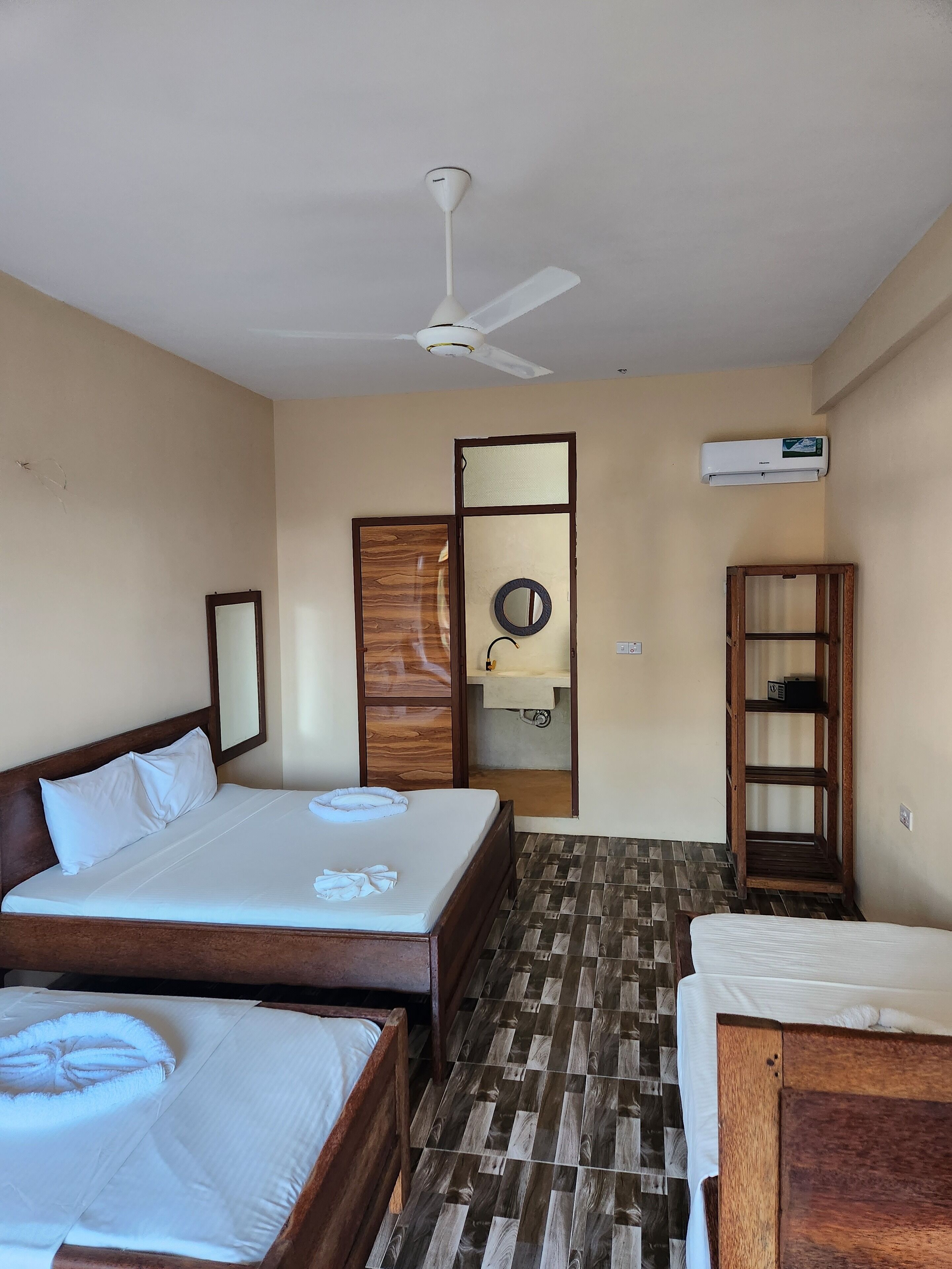 Camera d'albergo con un letto, un letto aggiuntivo, una toeletta con specchio, un condizionatore d'aria e una mensola in legno.