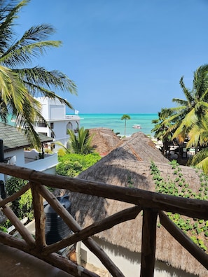 A beach view with a thatched-roof structure, palm trees, and a clear blue sky. - Two Palms (Jambiani)