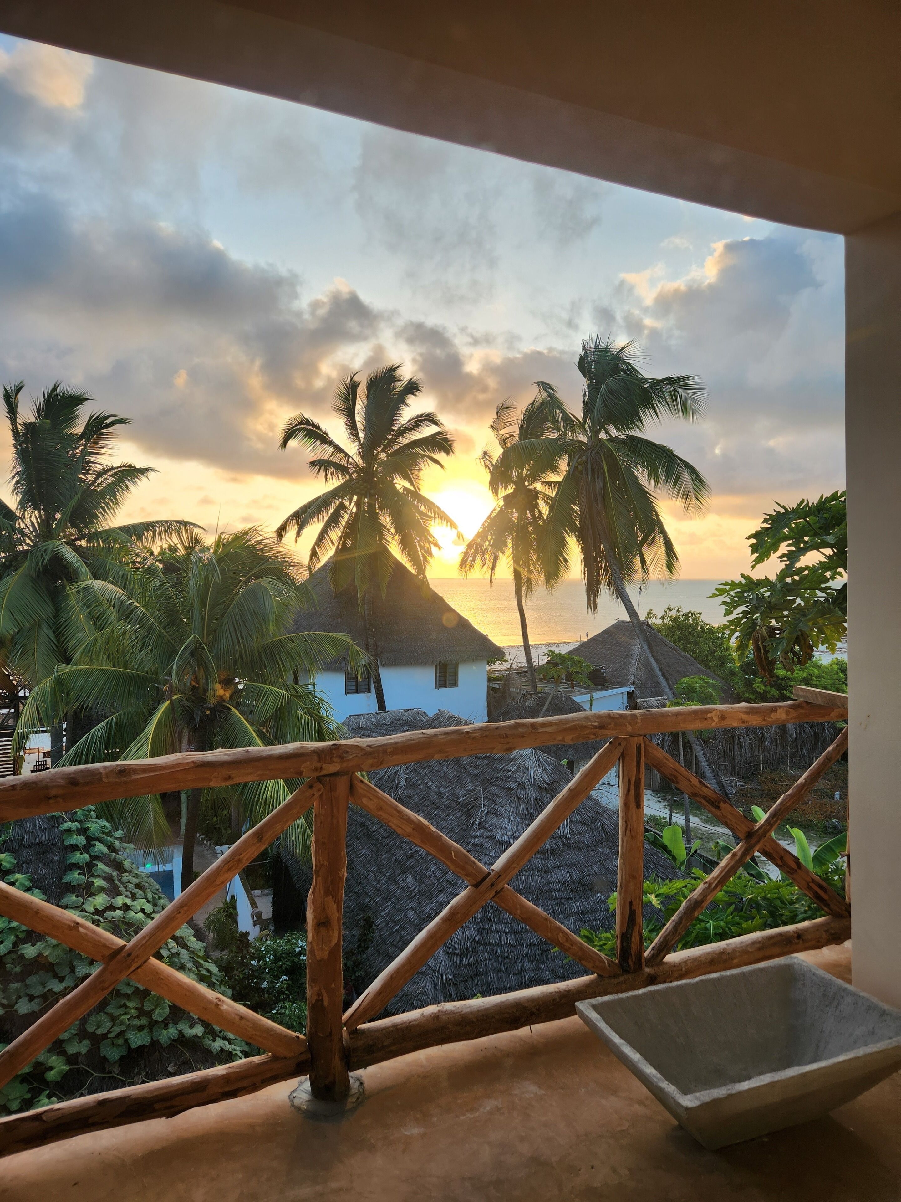 A balcony with a view of palm trees and a sunset.