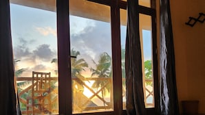 Ein Zimmer mit einer großen Schiebeglasdoor zum Balkon mit Blick auf Palmen und einen Sonnenuntergang.