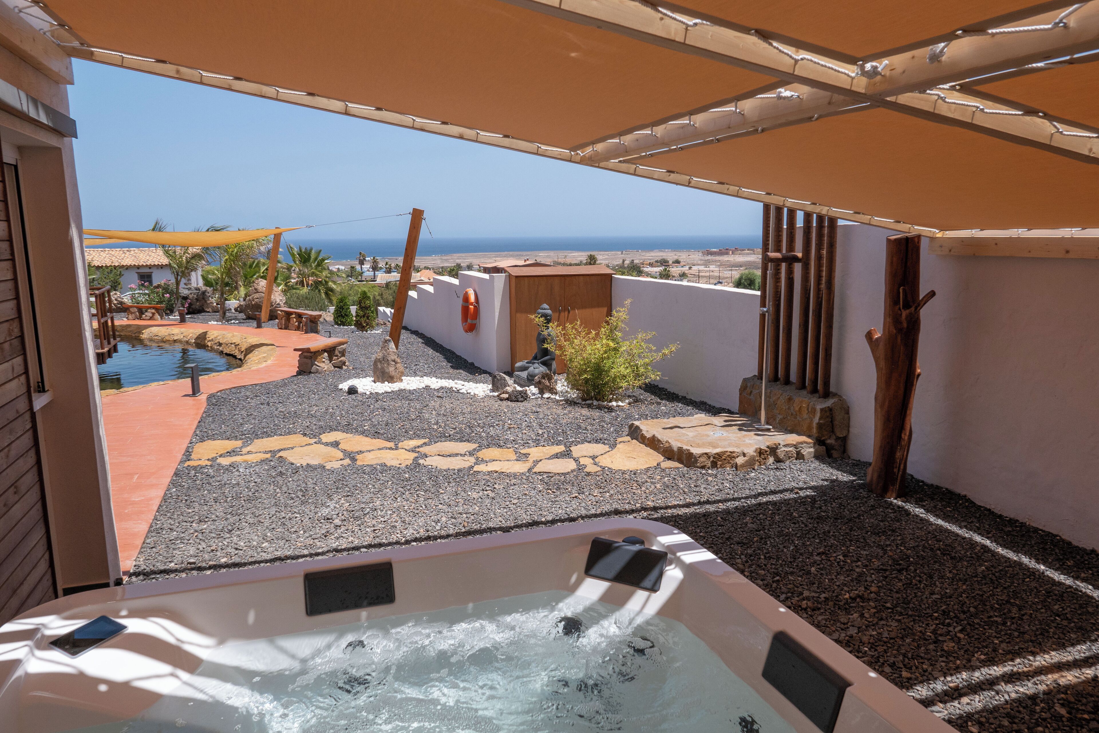 Uma banheira de hidromassagem com vista para o mar, rodeada por um espaço de pátio com deck de madeira, uma piscina pequena e um caminho de pedra.