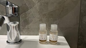 A bathroom sink with a chrome faucet and two bottles of Aura Intimate Care on the counter. - Calua Luxury Rooms (Agrigento)