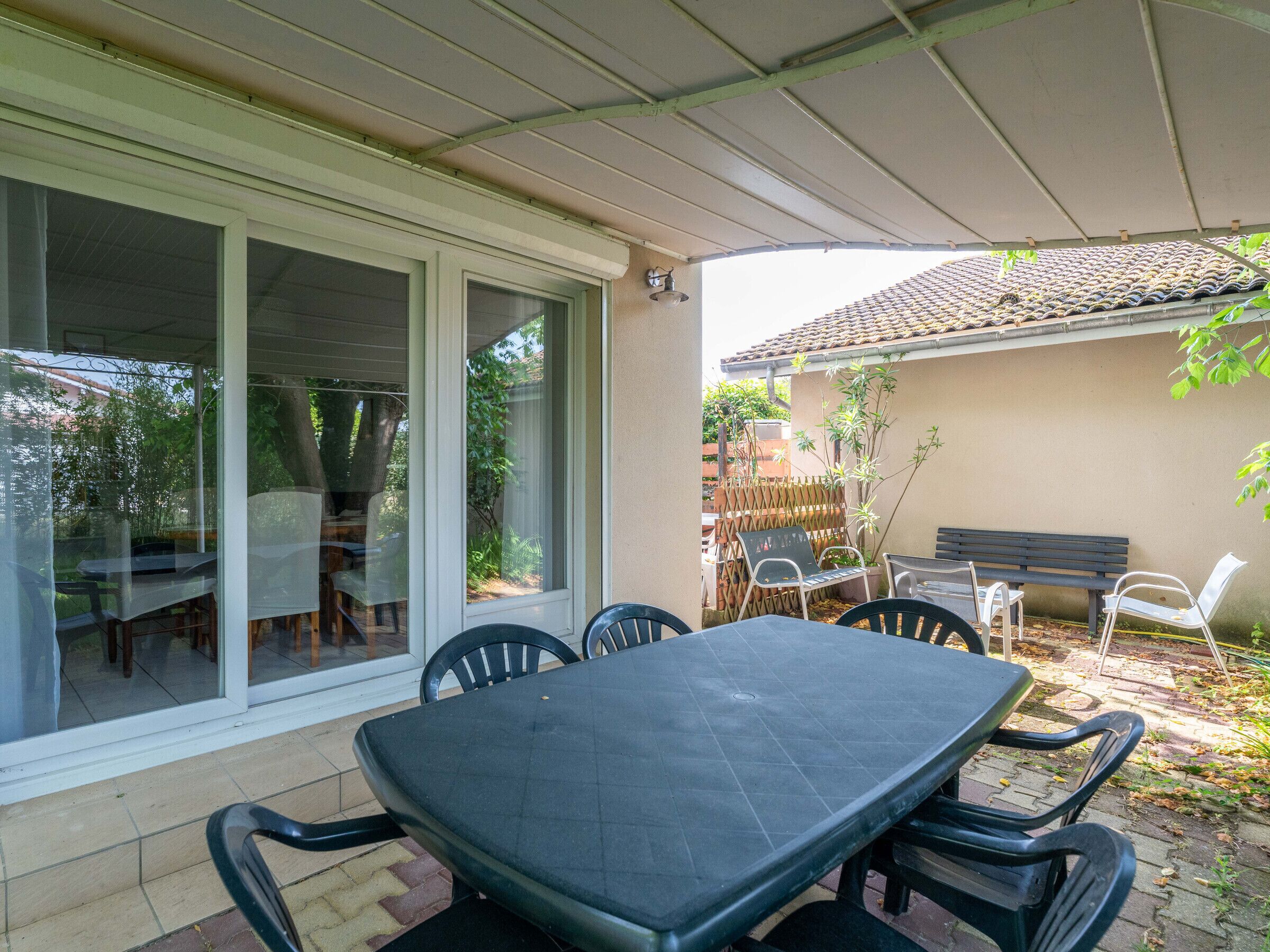 A patio with a table and chairs, a sliding glass door, and a covered area with a bench and chairs.