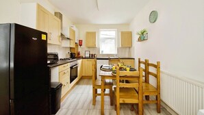 A compact kitchen with wooden cabinets, a black refrigerator, and a dining table with chairs. - The Green Garden House -Stunning large house near Shopping centre, Finsbury Park (Greater London)