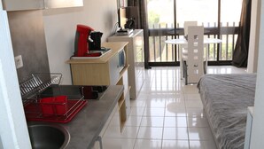 A hotel room with a bed, a kitchenette with a sink, a coffee machine, and a balcony with a table and chairs. - Charming Studio for 2 with Pool Access, Renovated, Parking, Near Beach (Cap d'Agde naturisme)