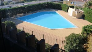 A rectangular swimming pool with a tiled deck, surrounded by a low brick wall and greenery. - Charming Studio for 2 with Pool Access, Renovated, Parking, Near Beach (Cap d'Agde naturisme)